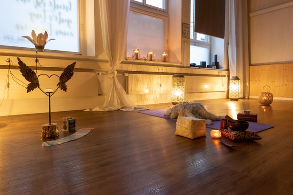 Abendlicher Yoga-Raum mit brennenden Kerzen, Engelsflügel-Deko und vorbereiteten Plätzen